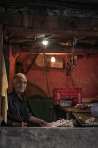 A senior butcher smiling while preparing meat in a dimly lit workshop.