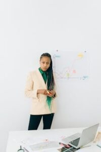 Businesswoman analyzing charts in an office setting with a laptop and diagrams.