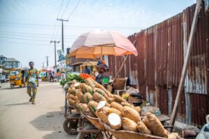 Colorful street market scene in Lagos, Nigeria, featuring a woman selling vegetables and yams.