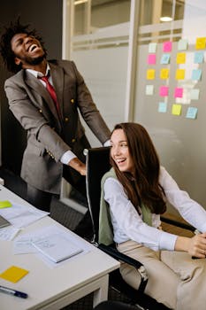 A cheerful office scene with colleagues laughing and engaging playfully around a desk.