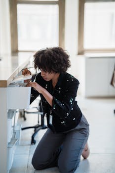A woman kneeling and searching in an office drawer, focused on finding documents.