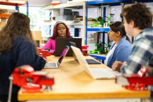 Diverse group of students engaged in a collaborative technical class discussion in a workshop setting.