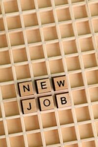 Overhead view of Scrabble tiles arranged to spell 'New Job' on a wooden grid background.