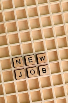Overhead view of Scrabble tiles arranged to spell 'New Job' on a wooden grid background.