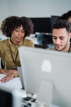 Two young adults working together on a computer in a modern office environment.